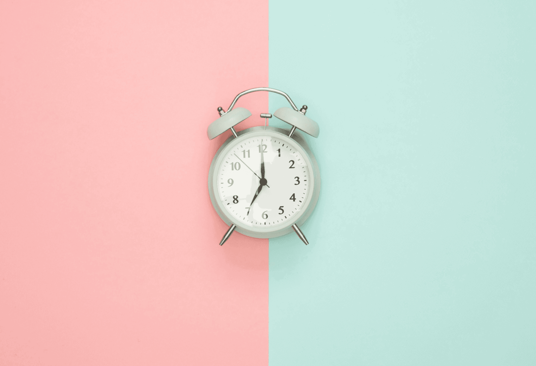 A close up image of an alarm clock on a background split in the middle with pink on the left and blue on the right